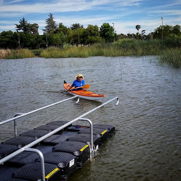 A person in an orange kayak paddles near the rubber kayak ramp