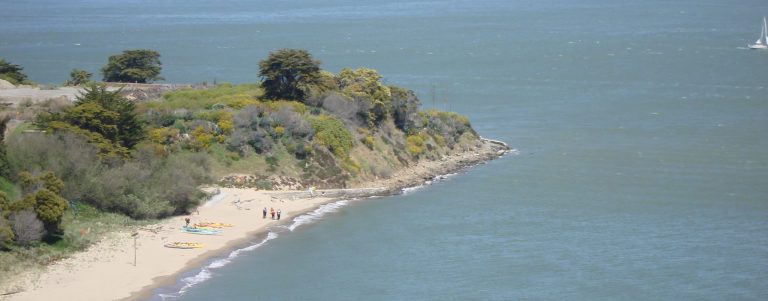 Distant view of beach with kayaks, and sailboats in the San Francisco Bay in the background