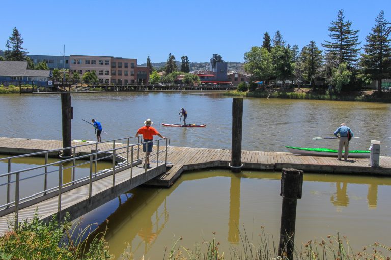People standing on the accessible ramp and dock with paddle boarder floating by