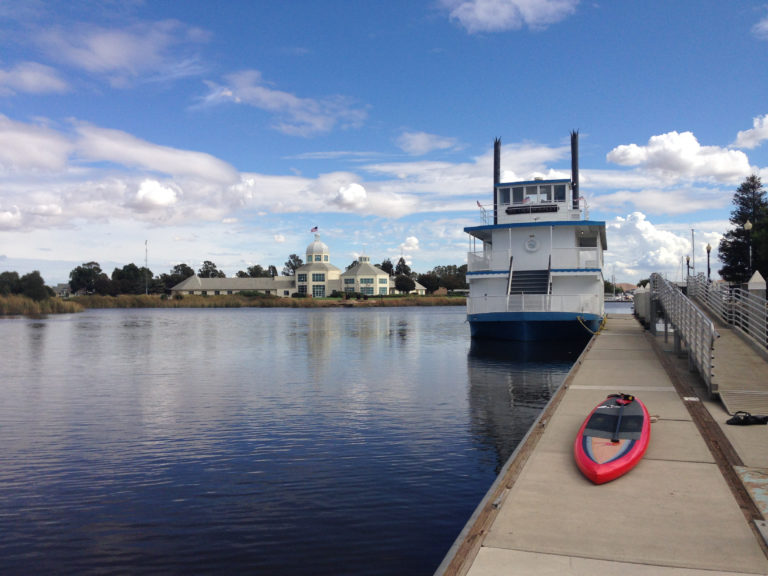 red paddleboard on dock and riverboat moored at dock with city hall in distance