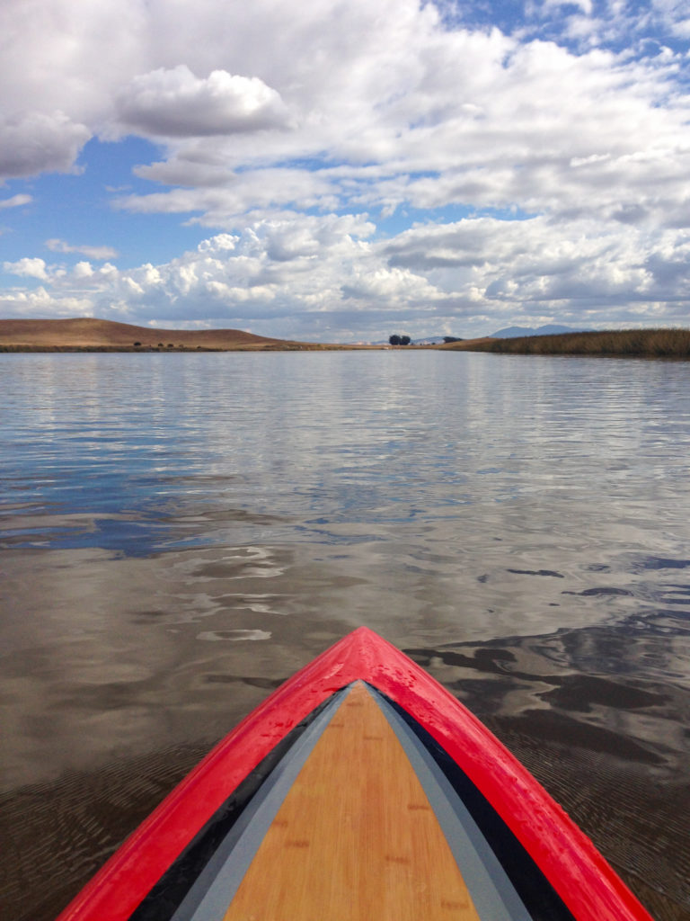 Paddleboard view across water with low brown hills in the distance
