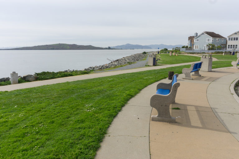 Benches next to green grass and paved pathways, overlooking the bay
