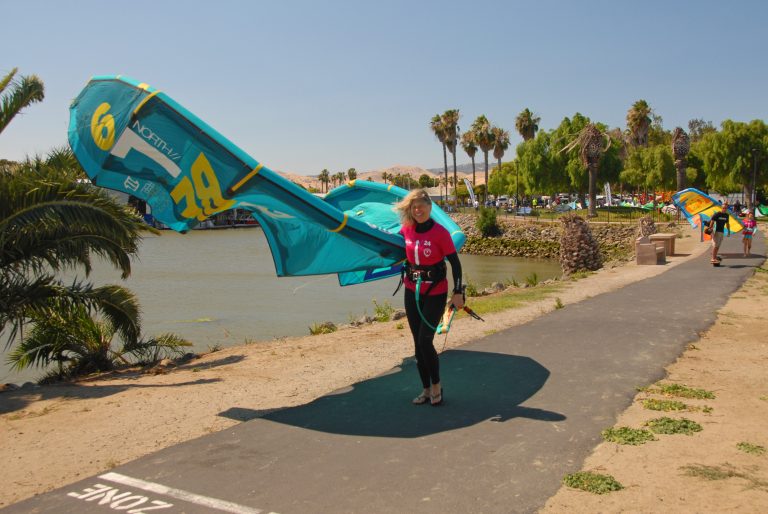 A woman walking on a paved path with a kiteboard kite under her arm