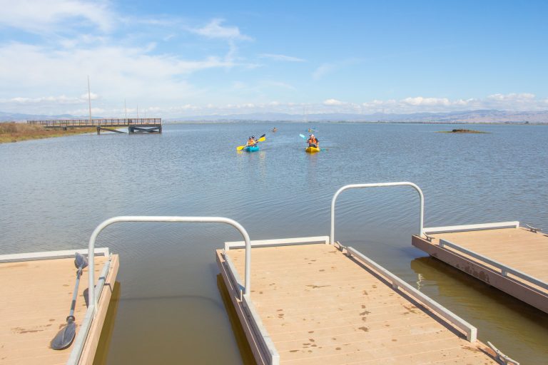 Low-freeboard docks with kayak berths and kayakers paddling in distance