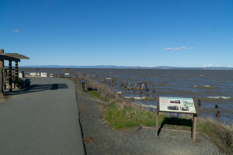 Signage next to a paved trail that winds along the shoreline