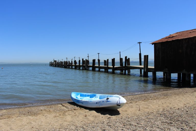 An empty sit-atop kayak on a beach with a pier in the background