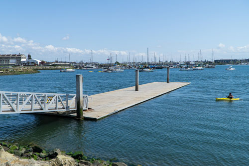A person in a yellow kayak approaches a low-freeboard dock